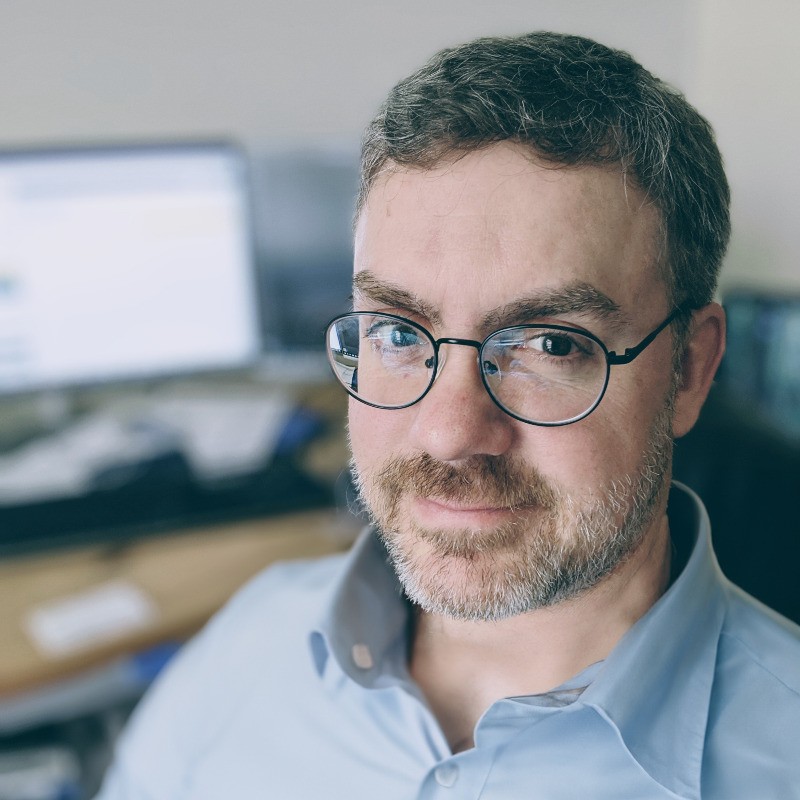 Jimmy Longley posing in front of computer monitors, wearing a dress shirt.